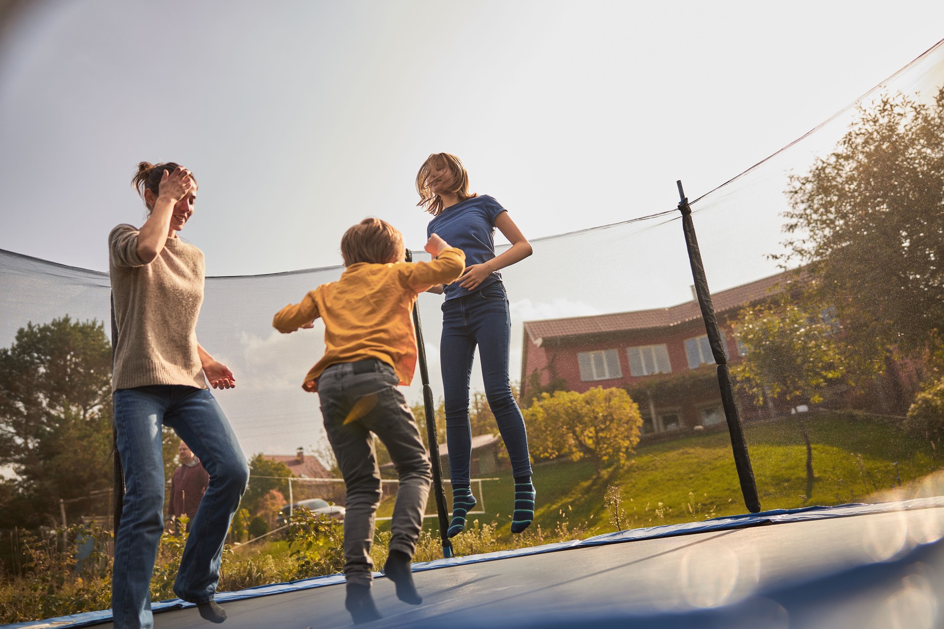 happy family are jumping on trampoline at backyard of their cozy home at summer sunset