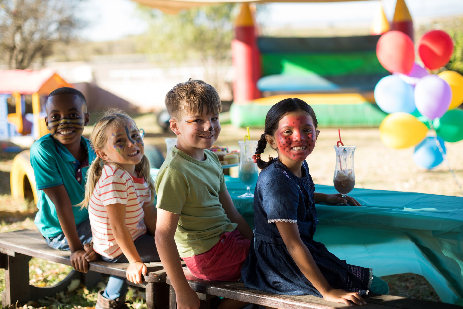 Happy friends with face paint having drinks while sitting on bench at park